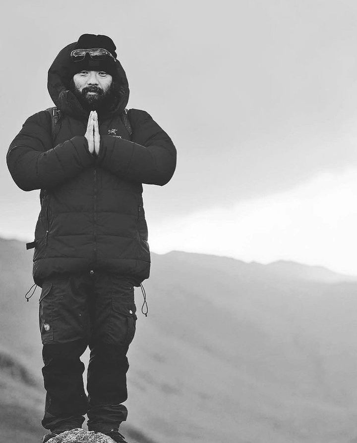 Krishna Thapa with his palms pressed together on a mountainside