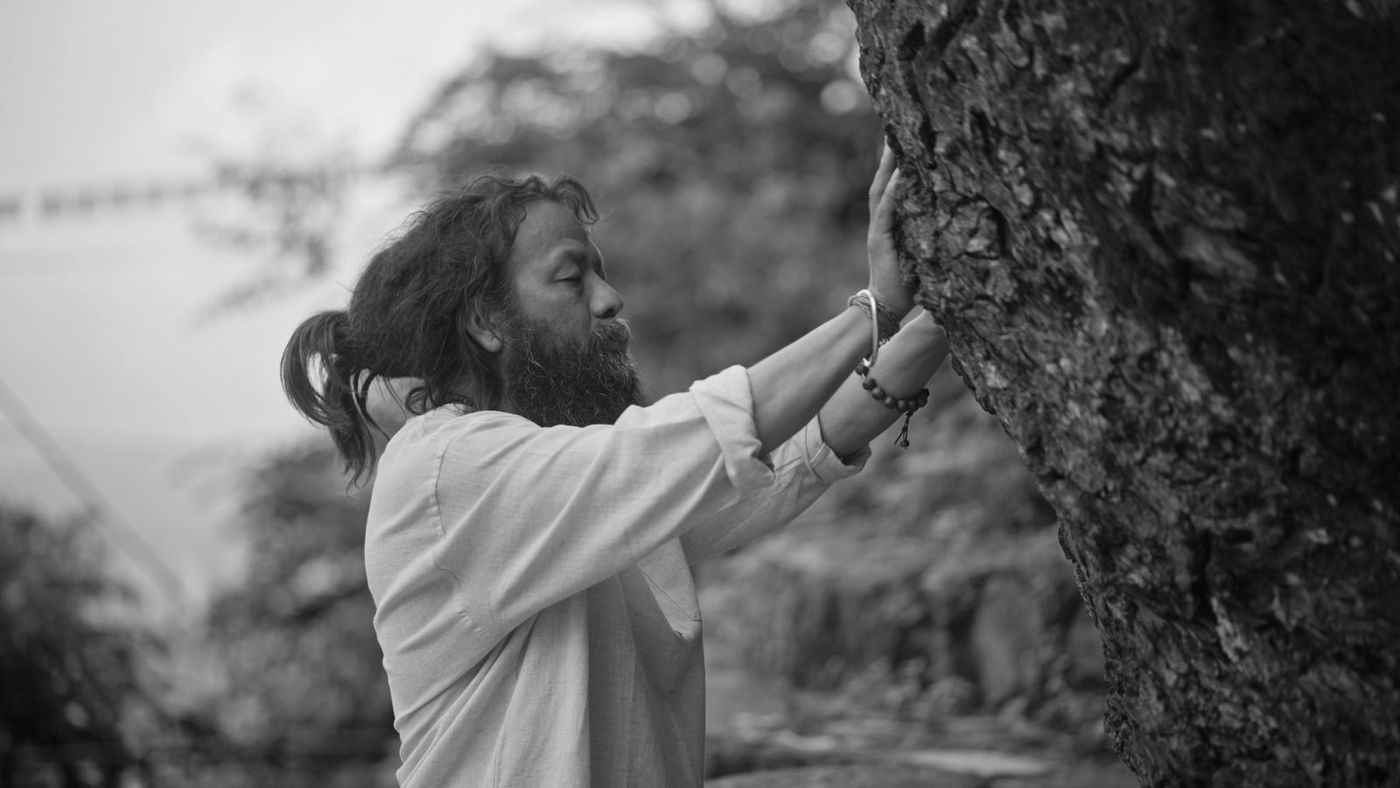 Krishna Thapa with both hands on the trunk of a tree, eyes closed